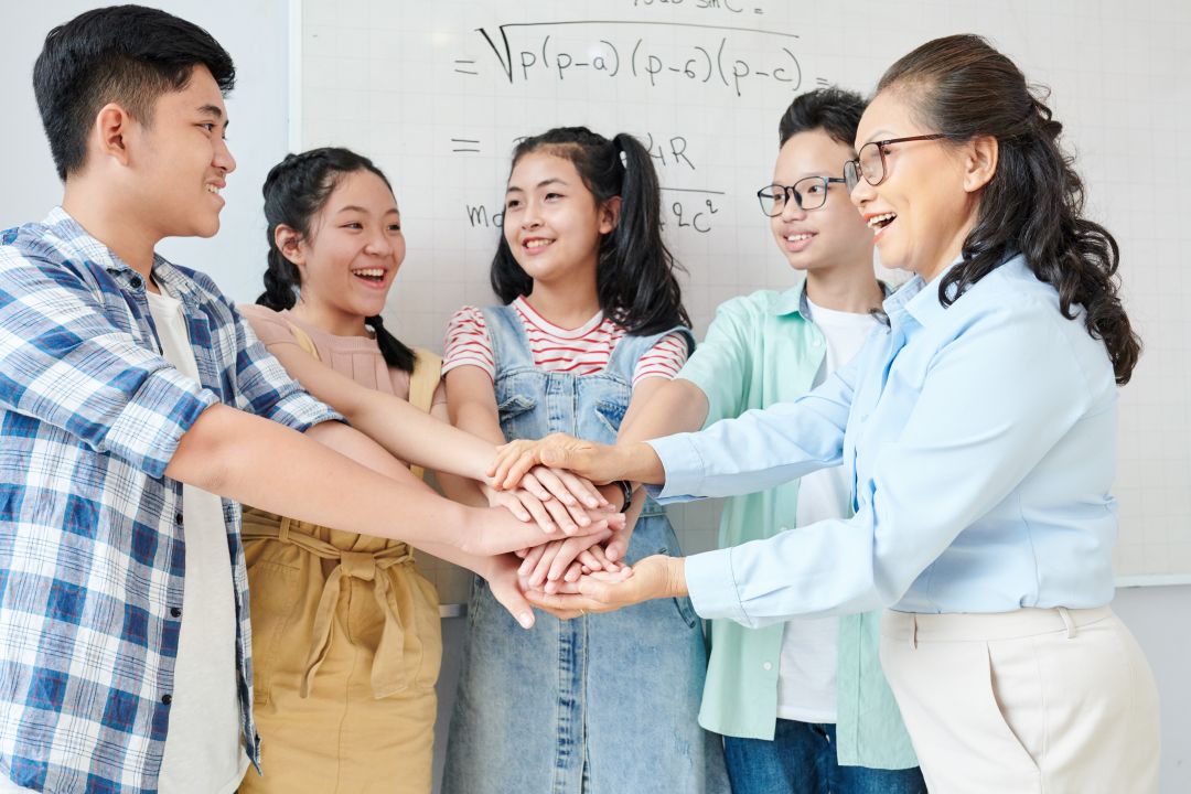 Secondary School Students stacking hands with their mathematics tutor